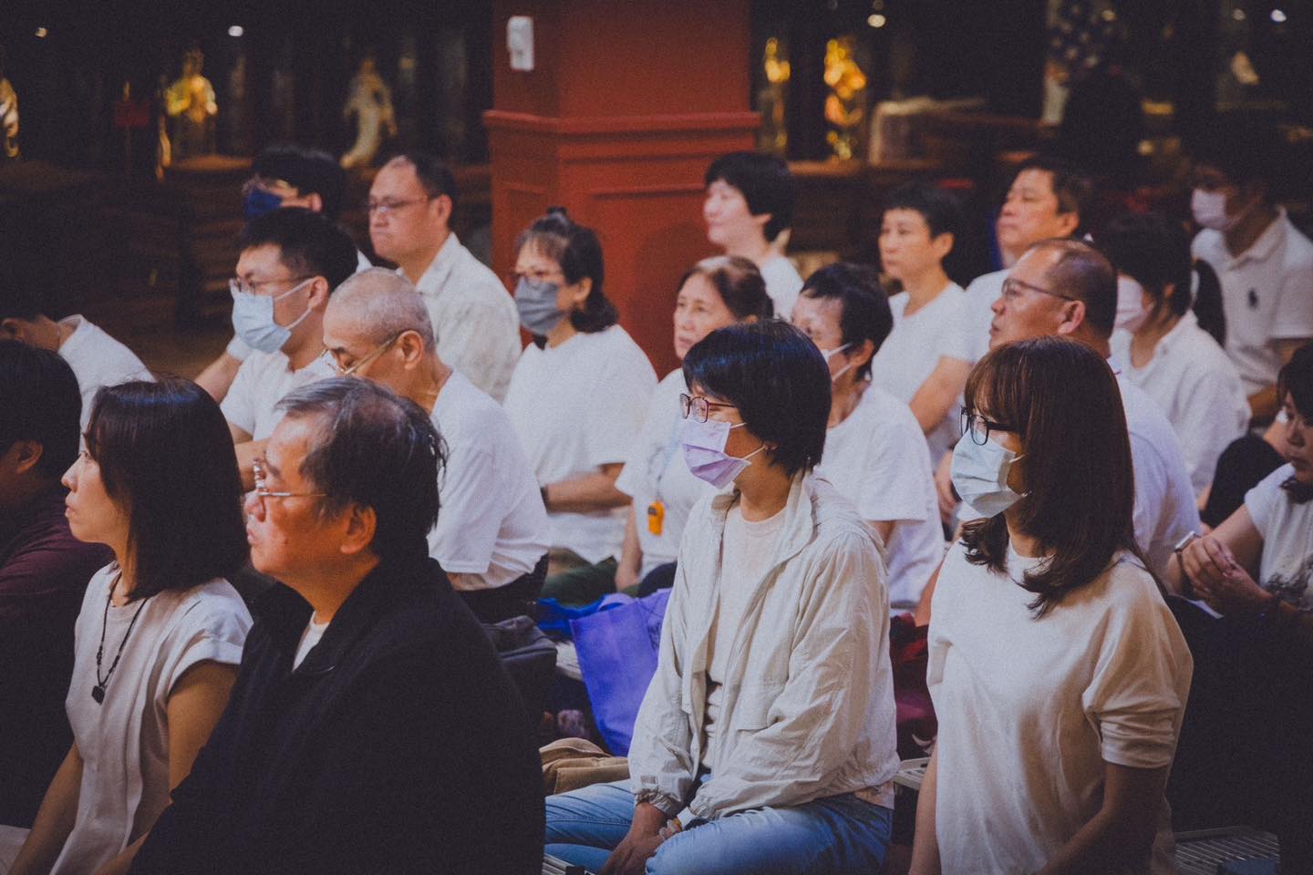 從後方拍攝，滿座參與者面向明亮供壇。