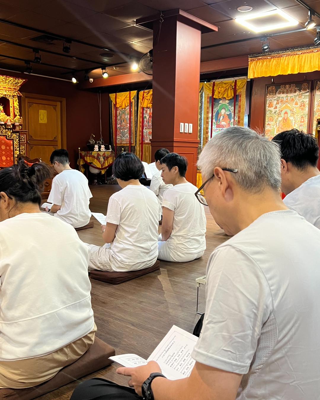 佛堂一角,參與者手持經本坐地誦讀。