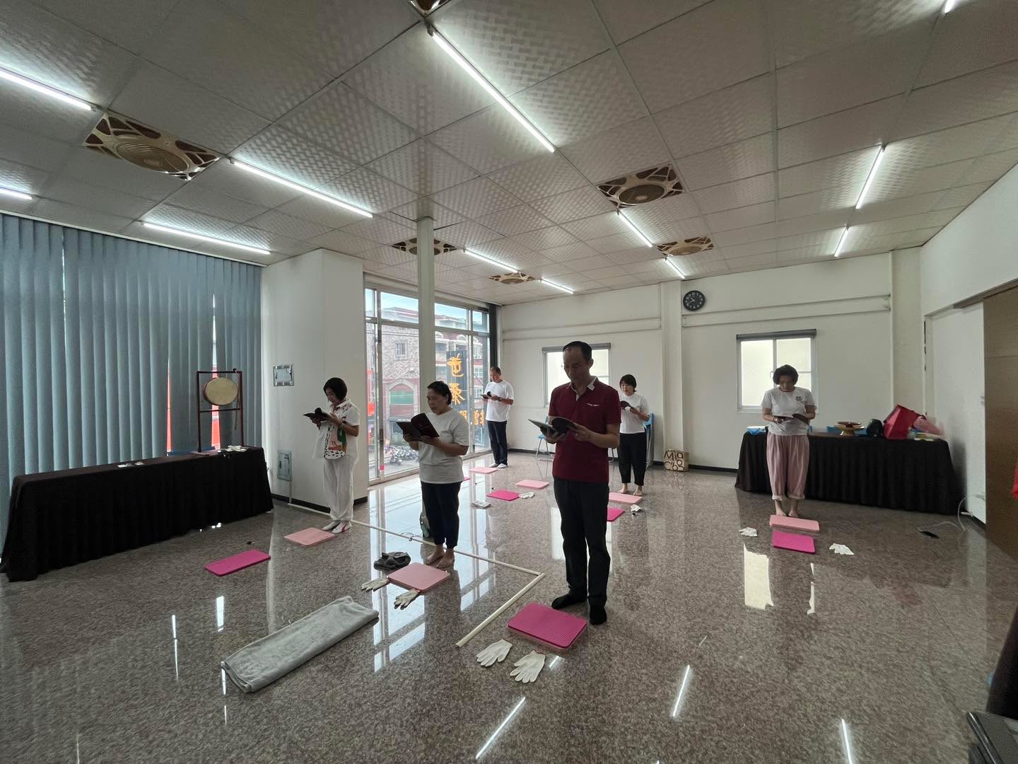 室內窗邊，多位參與者在跪墊前站立共修。